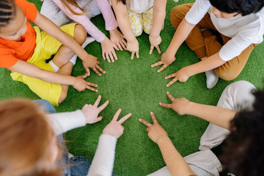A Group of kids sitting in a circle making peace signs
